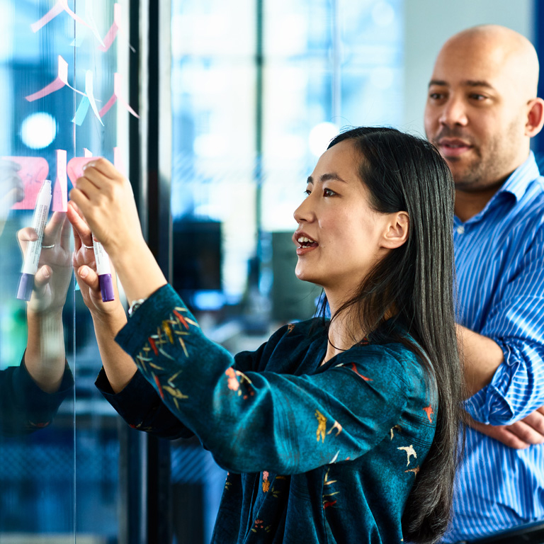 Candid portrait of attractive businesswoman brainstorming with colleague, using adhesive notes for planning and strategy